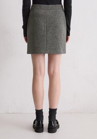 Grauer Wollmischrock mit tailliertem Schnitt, mittlerer Oberschenkel-Länge und klaren Linien. Kombiniert mit schwarzen Schuhen und dunkelgrauen Socken.