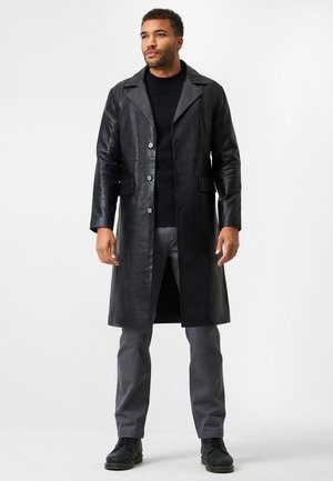 Schwarzer Leder-Langmantel mit Reverskragen, vorderen Knöpfen, zwei Taschen und einer glatten Textur, kombiniert mit grauen Hosen und schwarzen Schuhen.