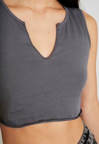 Top corto gris con escote en V, hecho de suave material de algodón, con costuras de borde sin terminar a lo largo del dobladillo y del cuello.