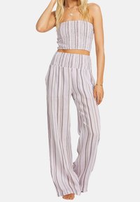 Gorsetowy top bez ramiączek i spodnie o szerokich nogawkach z lekkiego materiału, z pionowymi paskami w kolorach lawendowym i kremowym z brązowymi akcentami.