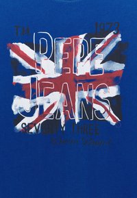 Sininen puuvillapaita, jossa on Union Jack -graafinen kuva. Teksti lukee "Pepe Jeans Seventy Three" suurilla valkoisilla ja mustilla kirjaimilla.