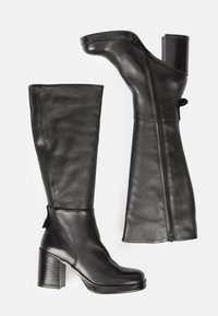 Bottes noires en cuir montant jusqu'au genou, avec un talon bloc épais, une fermeture éclair latérale et une finition lisse ; elles présentent un bout arrondi et un design minimaliste.