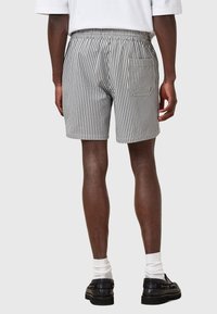 Pantaloni corti a righe in misto cotone con vita elastica, tasca posteriore e vestibilità rilassata. Strisce verticali bianche e nere con finitura testurizzata.