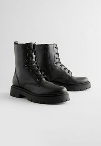 Zwarte enkellaarzen van textuurleer. Voorzien van vetersluiting aan de voorkant, zijrits en een chunky rubberen zool met een grof patroon.