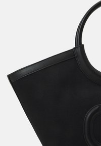 Černá taška typu tote s texturovaným plátnovým tělem, hladkými koženými doplňky, strukturovaným tvarem a zaobleným držadlem.