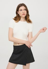 Maglione bianco corto con maniche corte, realizzato in materiale peloso; abbinato a una gonna nera con sottili righe bianche verticali.