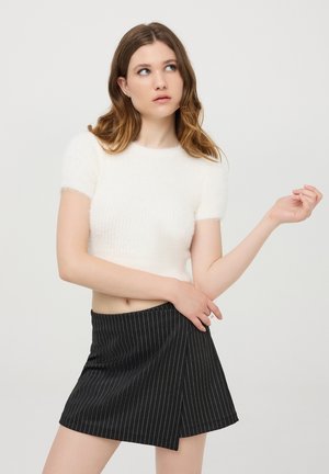 Maglione bianco corto con maniche corte, realizzato in materiale peloso; abbinato a una gonna nera con sottili righe bianche verticali.