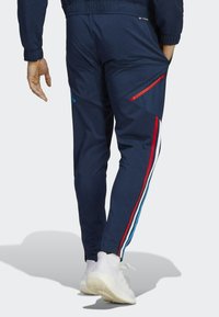Navy atletische broek met rode en blauwe accenten, voorzien van ritszakken aan de zijkanten en taps toelopende pijpen. Lichtgewicht, gladde stof met elastische tailleband.