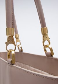 Borsa in pelle rosa chiaro con hardware dorato, caratterizzata da due manici strutturati e attacchi a clip. L'interno presenta una fodera a motivo.
