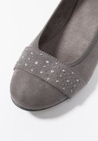 Scarpa in suede grigio piatto con texture liscia, caratterizzata da una fascia decorativa di piccoli strass luccicanti nell'area delle dita.