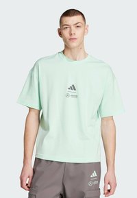 Svijetlo zeleni kratkodlaki pamukasti majica s printanom crnom adidas logotipom i Mercedes brendingom na prednjoj strani.