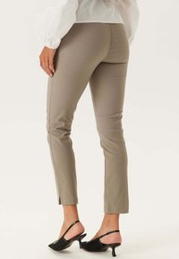 Beige aansluitende broek met een gladde textuur, een middelhoge taille en zijsplitten aan de zoom, gecombineerd met zwarte hakken.