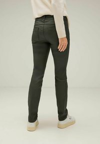 Mörkgröna, slim-fit byxor i stretchmaterial, med midjehöjd och bakfickor. Bärs med vita sneakers.