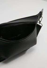 Bolso de hombro sintético negro con un compartimento con cremallera, con herrajes plateados y textura suave, parcialmente abierto para revelar su interior.