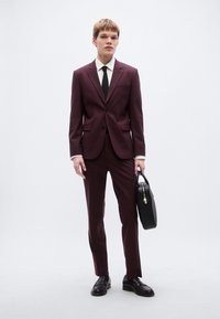 Μπορντό κοστούμι με εφαρμοστή γραμμή, σακάκι με ένα κουμπί, μαύρη γραβάτα και λευκό πουκάμισο. Μαύρη δερμάτινη χαρτοφύλακα και παπούτσια. Ομαλή υφή, σύγχρονος σχεδιασμός.