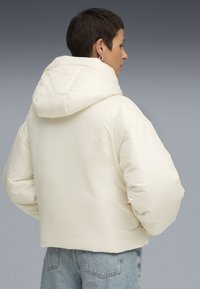 Puffjacka i off-white med quiltad textur, oversize huva och voluminösa ärmar. Styling med ljusblå högmidjade jeans.