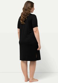 Vestido negro de manga corta con un corte holgado, que presenta aberturas laterales y un escote relajado, confeccionado en una tela suave y elástica.