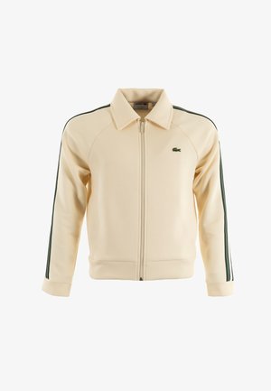 Cremfarbener Zip-Jacke mit grünen Streifen an den Ärmeln, gerippten Bündchen und Kragen. Mit Lacoste-Logo auf der Brust. Hergestellt aus weichem Stoff.
