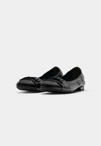 Une paire de ballerines en cuir noir avec des orteils ronds et des boucles décoratives, présentées sur fond blanc.