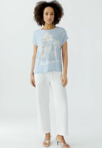 Hellblaue Kurzarm-T-Shirt mit einem Palmen-Graphic, kombiniert mit weißen weit geschnittenen Hosen und silbernen Absatzsandalen. Minimalistisches Design.