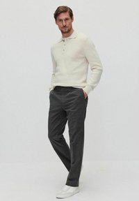 Cremekleurige gebreide polo met drie knopen, in combinatie met donkere grijze formele broeken en witte sneakers. Eenvoudig, goed passend ontwerp.