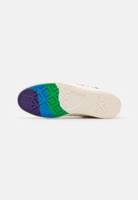 Semelle d'une basket blanche avec des sections en caoutchouc texturé violet, bleu, vert et blanc cassé en dessous pour l'adhérence et le style.