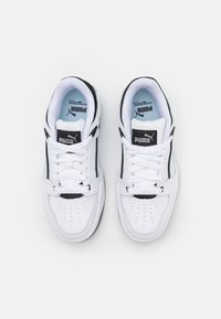 Paire de baskets Puma blanches et noires avec lacets, zone perforée au bout, et étiquettes de languette de marque, vues de dessus sur un fond clair.