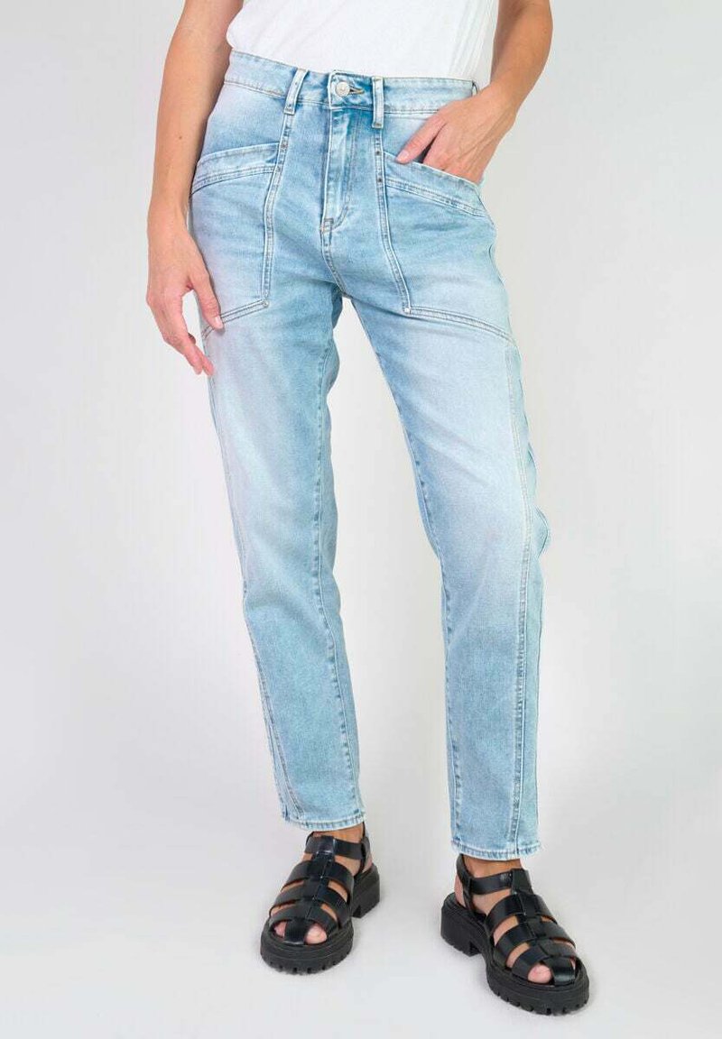 Jeans en denim bleu clair avec une taille haute, un design à jambe droite et des poches avant proéminentes. Portés avec des sandales noires à lanières.