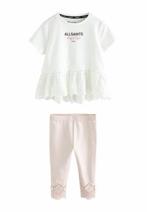 Fehér, pamutból készült póló lyukacsos fodros szegéllyel és fekete felirattal, rózsaszín leggingsszel párosítva, amely csipkés szegéllyel rendelkezik alul.