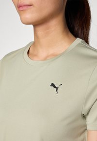 Ljusgrön sportt-shirt med rund halsringning, slät textur och en svart Puma-logotyp placerad på vänster bröst.