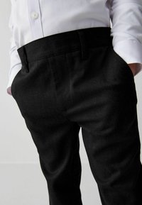Schwarze Hosen aus robustem Material mit glatter Textur. Verfügt über einen Bund mit Gürtelschlaufen und Seitentaschen, kombiniert mit einem weißen Hemd.