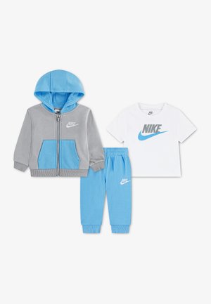 Veste à capuche zippée grise et bleue, pantalon bleu clair et t-shirt blanc à manches courtes avec logos Nike sur fond blanc.