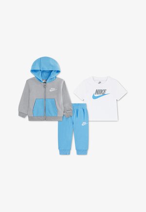 Veste à capuche zippée grise et bleue, pantalon bleu clair et t-shirt blanc à manches courtes avec logos Nike sur fond blanc.