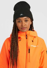 Lyst orange vandtæt jakke med en sort lynlås, høj krave og logo. Kombineret med en sort ribstrikket hue med et logopatch.