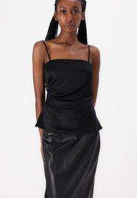 Camiseta de satén negro con tirantes finos y un diseño de peplum drapeado, combinada con una falda de cuero negro ajustada. Textura suave en toda la prenda.
