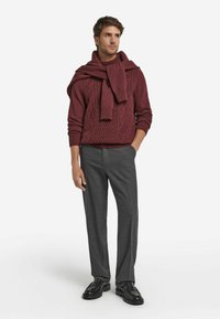 Bordeauxfarbener Strickpullover mit Zopfmuster, kombiniert mit grauen, maßgeschneiderten Hosen und schwarzen Lederschuhen. Schal über die Schultern drapiert.