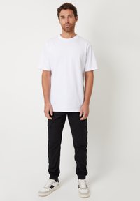 White cotton t-shirt, relaxed fit, short sleeves; paired with black cargo pants featuring side pockets; white and black sneakers.