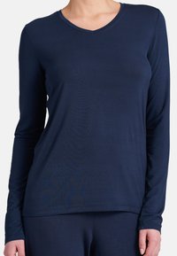 Mörkblå långärmad topp med v-ringning och en mjuk textur. Tyget faller lätt och har en svag lyster, med åtsittande ärmar.