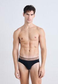 Zwarte katoenen boxershorts met een bruine Calvin Klein merkband; gladde textuur en een aansluitend ontwerp, model toont een vooraanzicht.