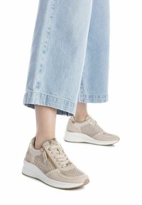 Zapatillas deportivas beiges con diseño perforado, puntera redondeada, acentos metálicos y una suela blanca acolchada. Combinadas con unos vaqueros cortos azul claro.