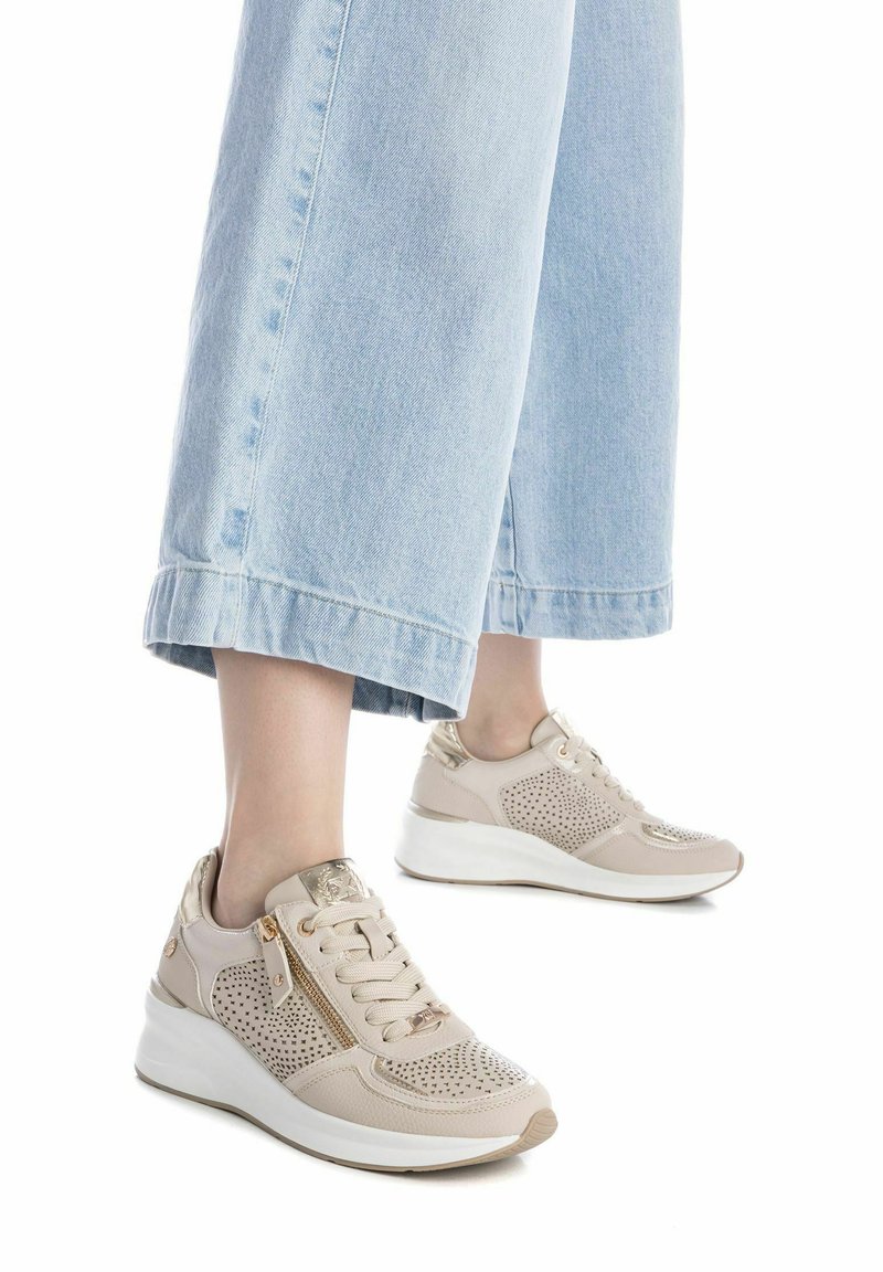 Zapatillas deportivas beiges con diseño perforado, puntera redondeada, acentos metálicos y una suela blanca acolchada. Combinadas con unos vaqueros cortos azul claro.