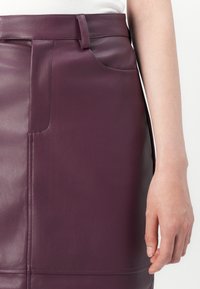 Lilla lædernederdel med en glat tekstur, diskret syning, sidelomme og tætsiddende design.
