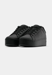 Černé platformové tenisky s hladkým, matným povrchem. Mají kulatou špičku, silnou podrážku a ploché tkaničky. Minimalistický design bez viditelného loga.