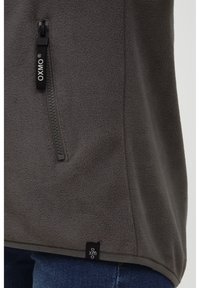 Chaqueta de forro polar gris con un bolsillo con cremallera, marca OXMO, textura suave y un ajuste relajado con detalle en la costura lateral.