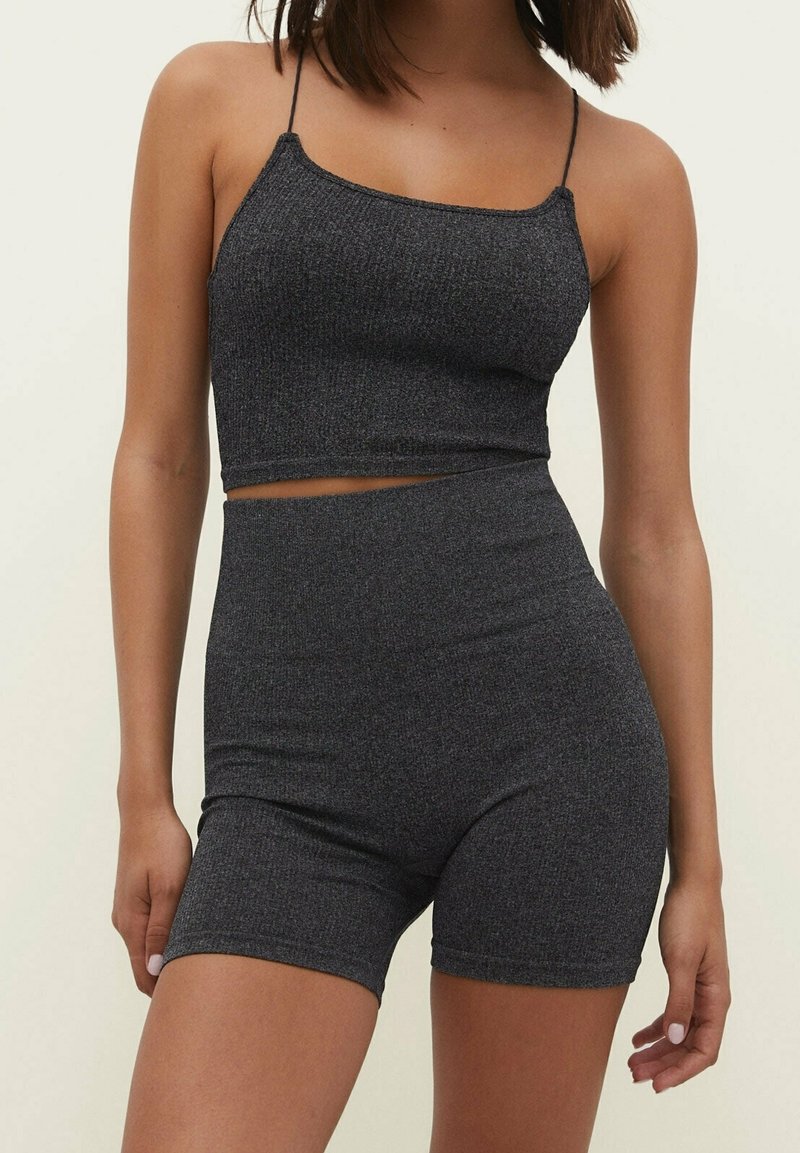 Mujer con una camiseta cropped de canalé gris oscuro de tirantes finos y un short de ciclista de talle alto a juego, contra un fondo liso.