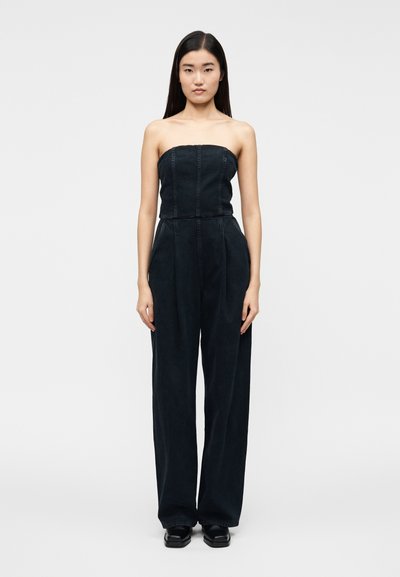 Combinaison bustier en jean foncé avec un corsage ajusté et un pantalon à jambes larges. Des coutures verticales ajoutent de la structure ; design minimaliste sans motifs.