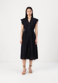 Melna pogu krekliņa kleita ar īsām viļņotām piedurknēm, jostu viduklī un viļņotu apakšmalu. Izgatavota no viegla auduma ar plūstošu siluetu.