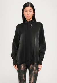 Black satin blouse with a tied neck detail, long sleeves, and a loose fit. Paired with patterned, form-fitting leggings featuring a snake-skin design.