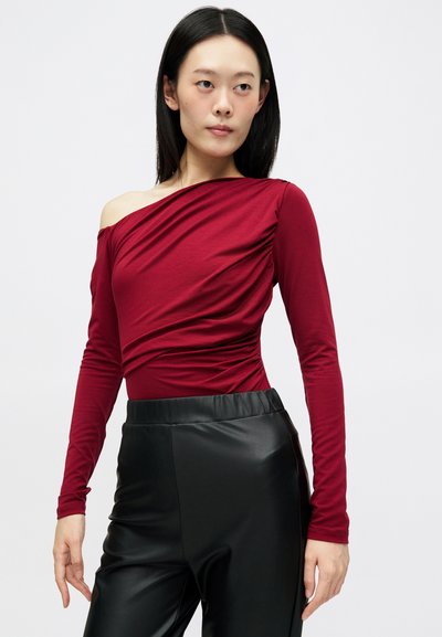 Top burgundy de ombro a descoberto com mangas longas, apresentando textura franzida e um design ajustado. Combinado com calças pretas de couro sintético de cintura alta.