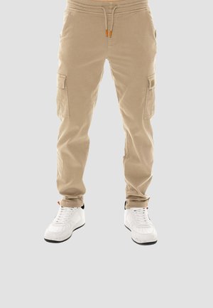 Beige Cargohose mit Seitentaschen und Kordelzugbund, getragen mit weißen Schnürsneakern auf hellem Hintergrund.